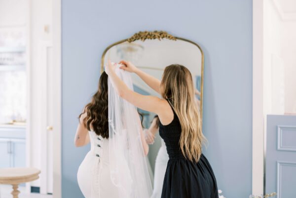 Stylist putting a veil on a bride who is wearing an aisle-ready bridal gown in front of a mirror at Bleu bridal Co