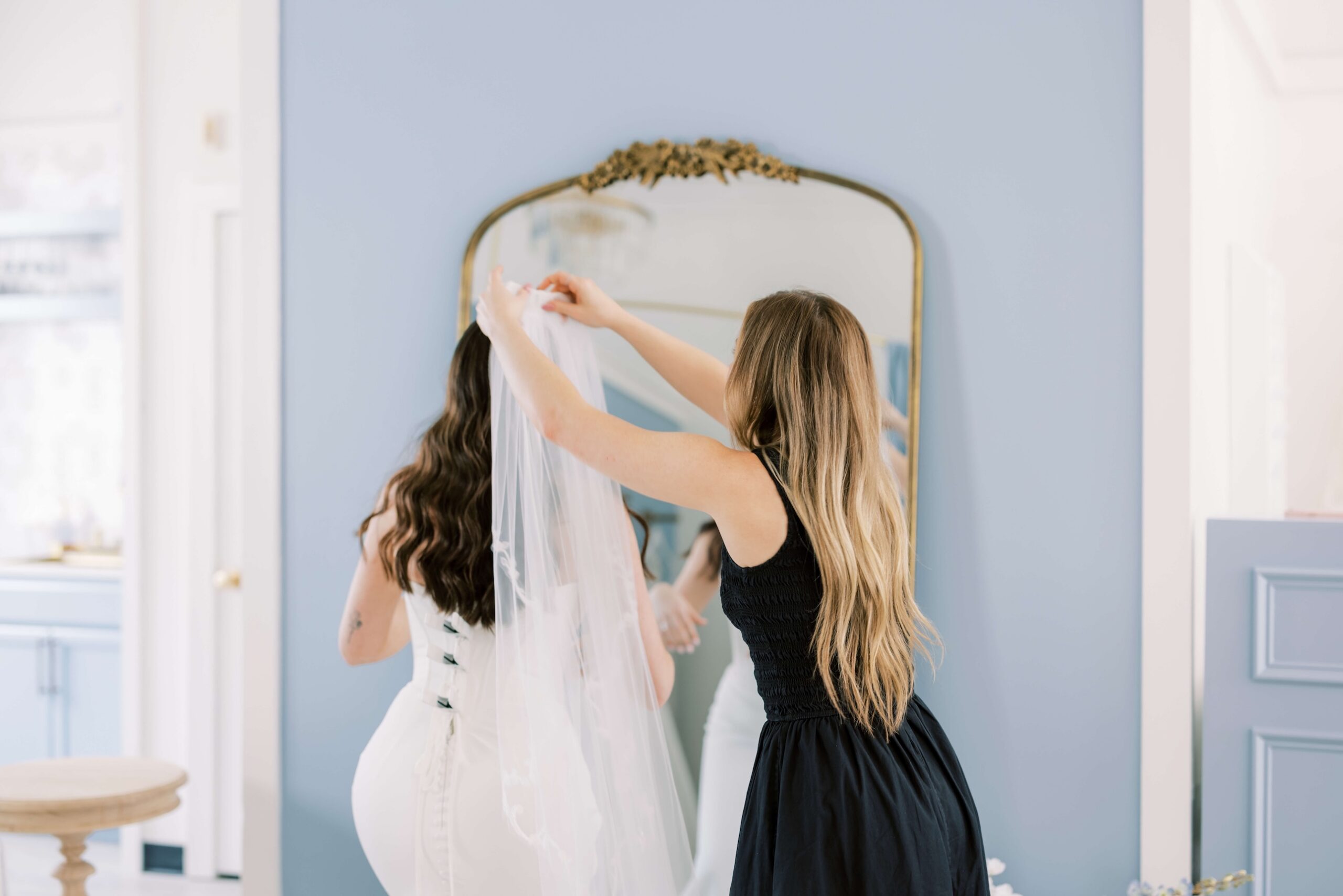 Stylist putting a veil on a bride who is wearing an aisle-ready bridal gown in front of a mirror at Bleu bridal Co